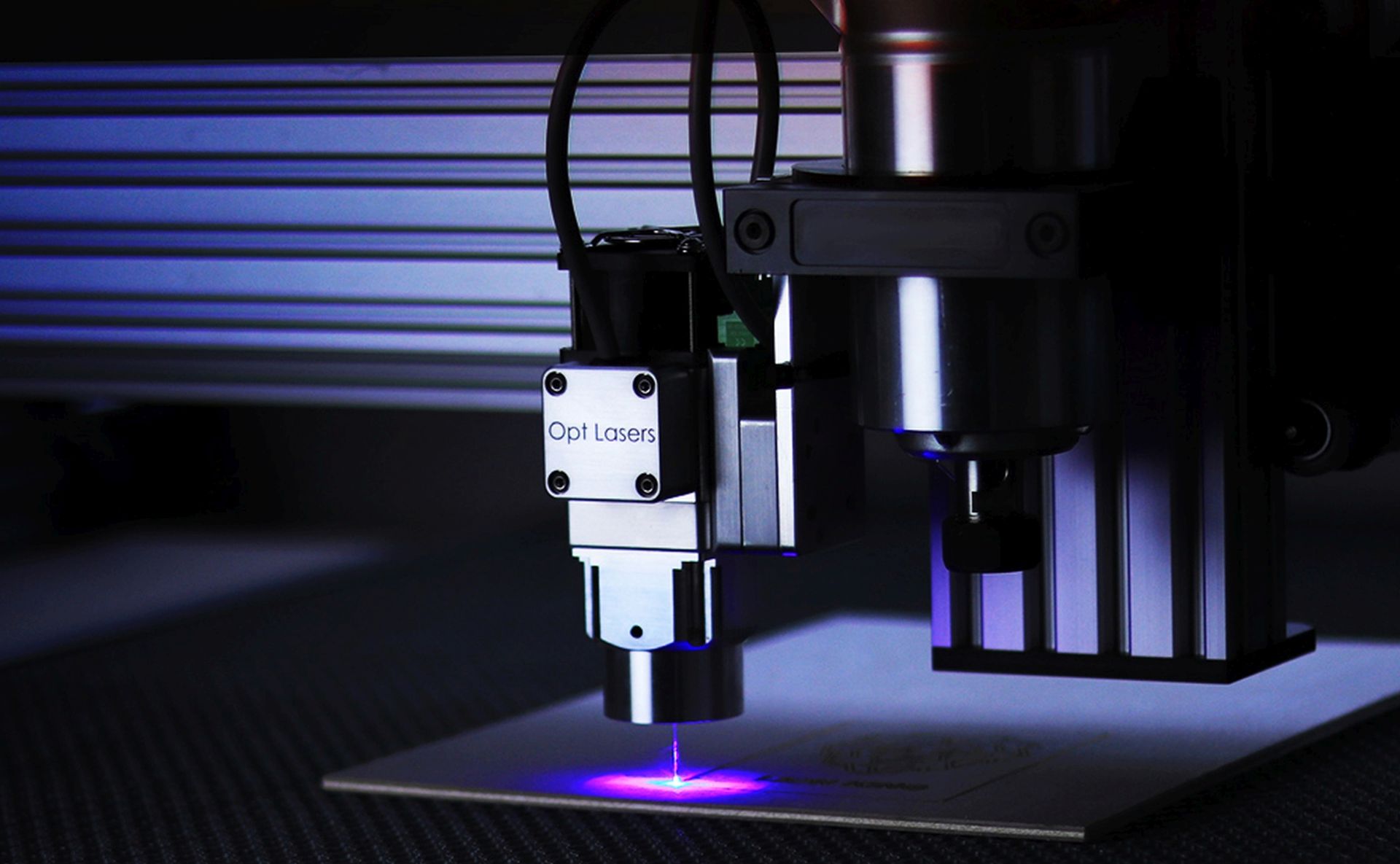 gros plan sur une tête de graveuse laser en fonctionnement, faisceau visible sur une pièce en cours de gravure