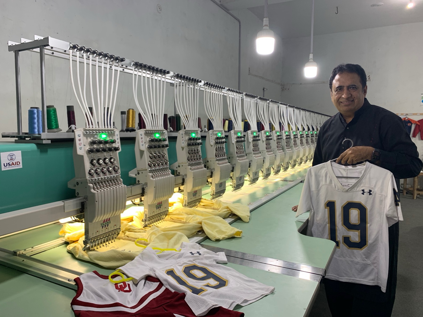 machine de broderie industrielle à plusieurs têtes brodant des maillots de sport numérotés, alignés sur le poste de travail